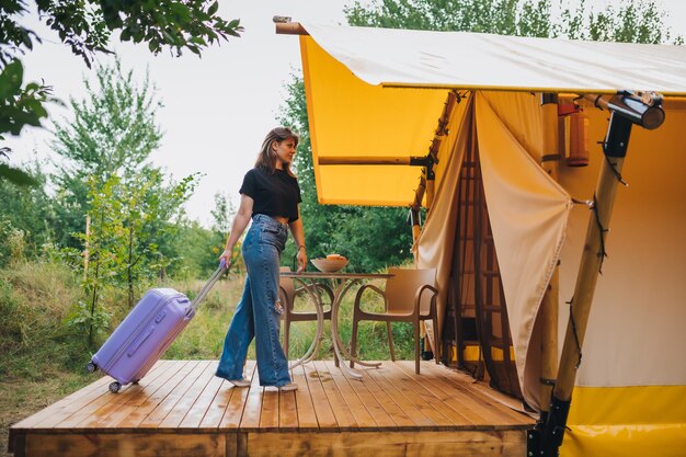 Woman traveler with luggage moving towards bedroom of cozy glamping house Luxury camping tent for outdoor summer holiday and vacation Lifestyle concept