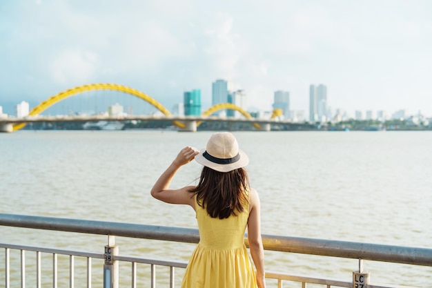 Woman Traveler with yellow dress visiting in Da Nang city Tourist sightseeing the river view with Dragon bridge Landmark and popular for tourist attraction Vietnam and Southeast Asia travel concept