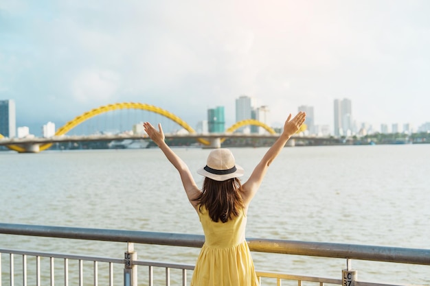 ダナン市を訪れる黄色いドレスを着た女性旅行者観光客がドラゴンブリッジで川の景色を観光し、ランドマークと観光名所で人気のあるベトナムと東南アジアの旅行コンセプト