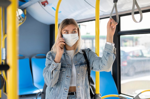 Женщина, путешествующая на общественном автобусе, разговаривает по телефону в медицинской маске для защиты