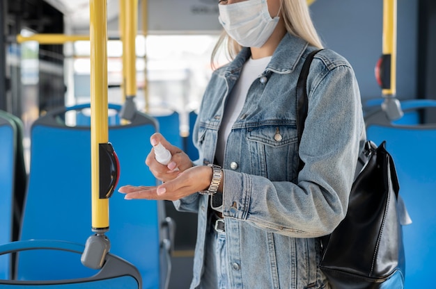 Woman traveling by public bus using hand sanitizer while wearing medical mask for protection