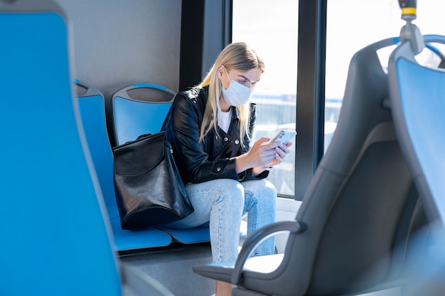 사진 보호를 위해 의료 마스크를 쓰고 스마트폰을 사용하여 대중 버스로 여행하는 여성