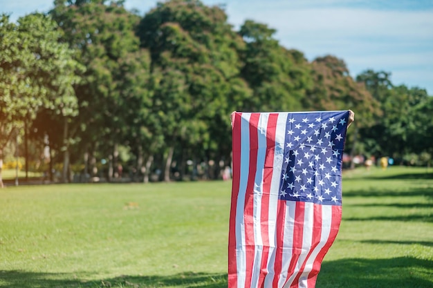 7月4日の退役軍人記念独立記念日と労働者の日のコンセプトの公園の屋外の米国の休日にアメリカ合衆国の旗を持って旅行する女性