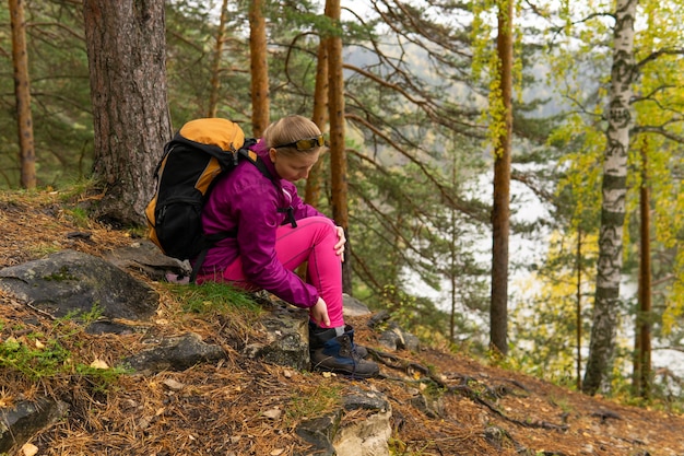 Woman trekker sitting on a mountain trail and holding on to a sore ankle