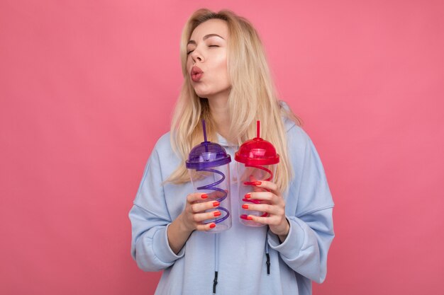 A woman in a trendy blue hoodie holds two cocktail glasses