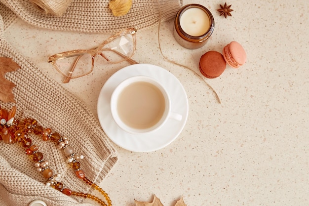 Woman trendy outfit sweater glasess and gemstone jewelery Autumn aesthetic coffee time among candle fall leaves macaroons Copy space