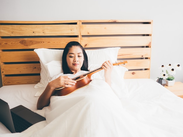Женщина пытается научиться укулеле в своей спальне.