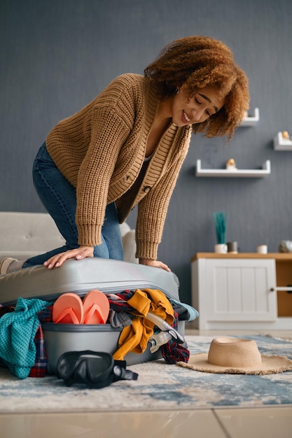 Donna che prova a chiudere la valigia di sovraccarico che spinge il coperchio preparazione per il viaggio in vacanza