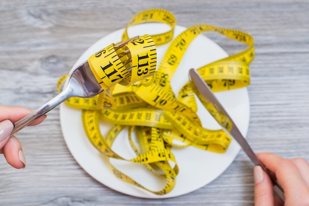 Woman trying to eat tape measure. Close up photo of tape measure on a plate and on a fork. Overhead view