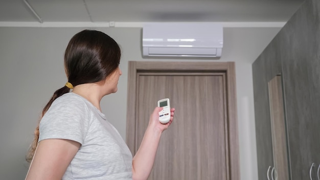 Woman turns on air conditioner with remote control in hot room