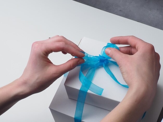 A woman tying a blue ribbon on a white box.