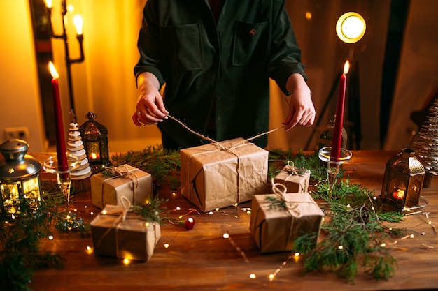 Woman tying holiday craft gift box with spruce branches on the wooden table