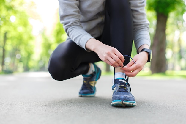 Donna che lega i lacci delle scarpe prima di correre, preparandosi per fare jogging nel parco, primo piano