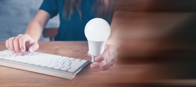 Woman typing on the keyboard holding a light bulb