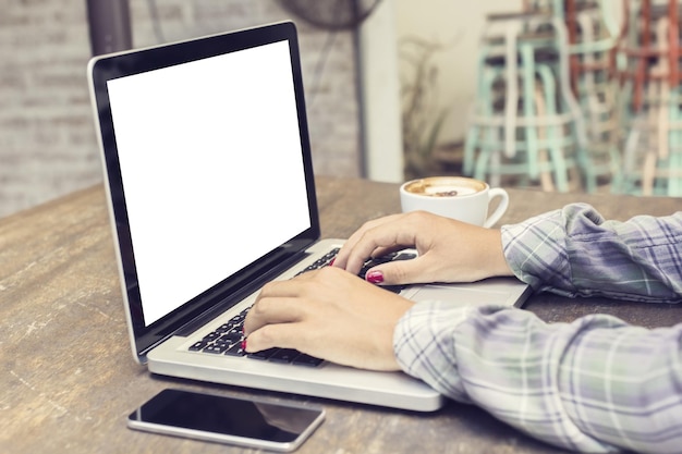 Woman typing on a laptop with cell phone and coffee mock up