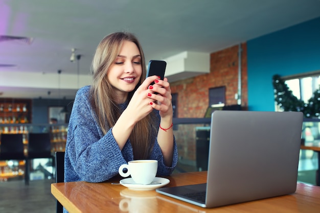 カフェでスマートフォンでテキストメッセージを入力する女性。