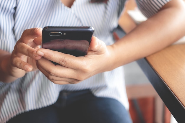 女性がカフェでスマートフォンでテキストメッセージを入力します。