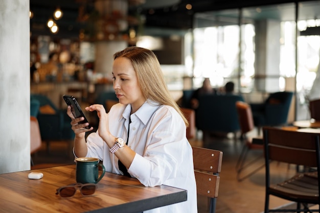 Woman typing text message on smart phone while sitting in a cafe