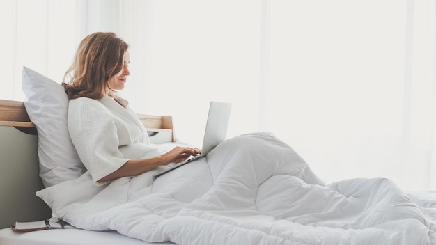 Woman typing work laptop on bed working in bedroom at home