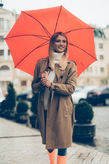 傘の下の女性。傘をさして、通りに立って笑っている魅力的な若い女性