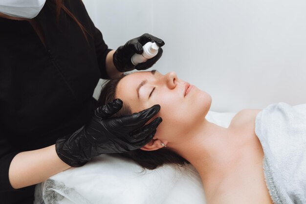 A woman undergoes a cosmetic procedure at the salon spa The cosmetologist puts the cream on the girl's face