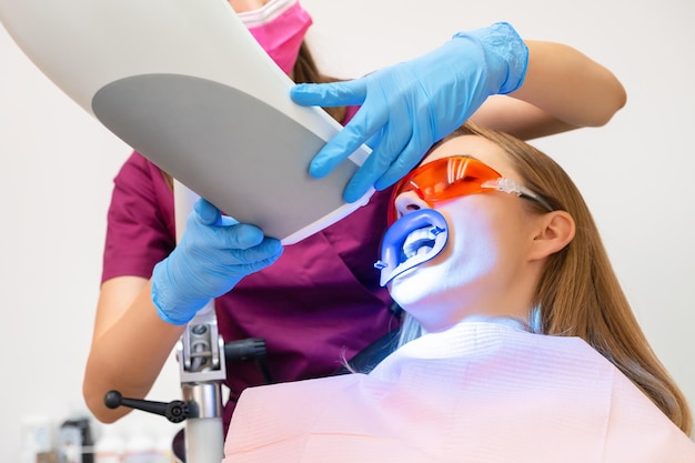 한 여자 는 치아 를 게 하고 자외선 램프 를 사용 하여 게 하는 과정 을 거치고 있다