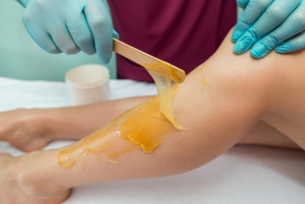 Woman undergoing leg hair removal procedure with sugaring paste in salon Skin care remove hair with sugar paste