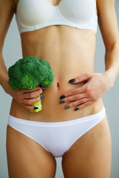 Woman In Underwear Holding a Bunch Of Broccoli And Touching her Stomach