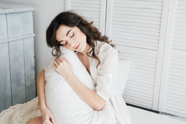 Woman in underwear sitting on the bed hugging a pillow