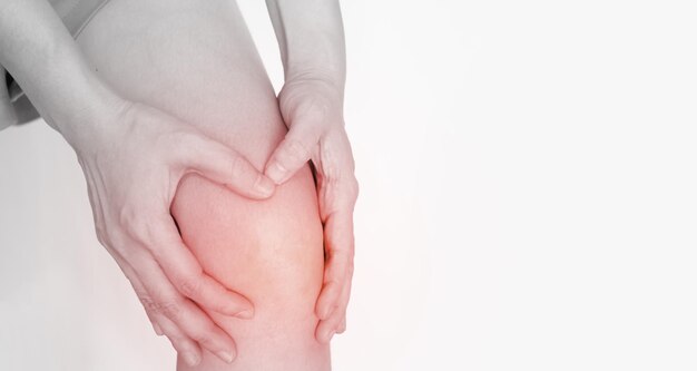 Женщина зажимает колено обеими руками, выражая боль и боль от ревматоидного заболевания или заболевания сухожилий