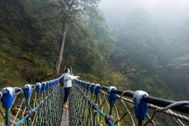 Woman use of camera to take photo with the pole walk though the suspension bridge in forest