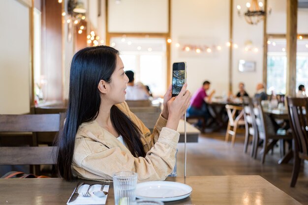 女性がレストランで携帯電話で写真を撮る