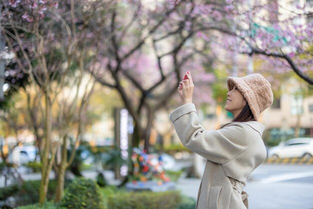 Woman use cellphone to take photo of sakura tree