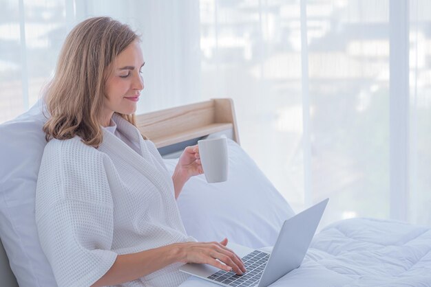 Woman use computer notebook on bed and drink coffee with copy space