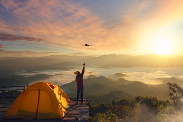 Photo a woman use drone for take a photo landscape between sunrise and fog background at top of mountain