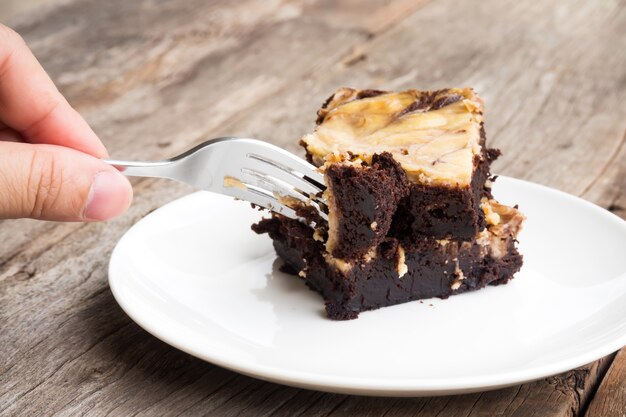 Woman use fork picking brownie cheese cake.