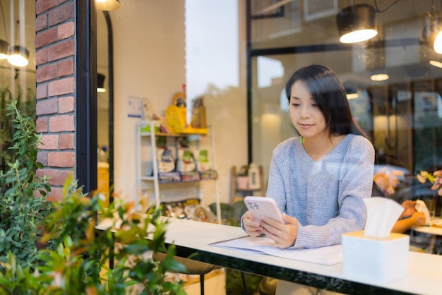 女性がコーヒーショップで携帯電話を使う