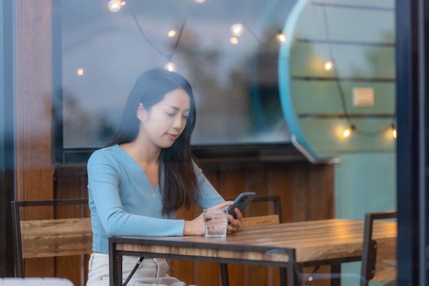 女性が携帯電話を使ってコーヒーショップの内側に座っています