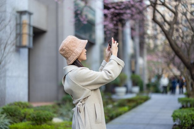 Woman use mobile phone to take photo in city with sakura tree