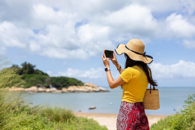 女性が携帯電話を使って海の写真を撮る