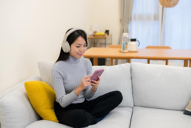 女性が家でヘッドフォンで携帯電話を使っている