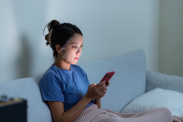 Woman use paper mask and look at the cellphone at home in the evening