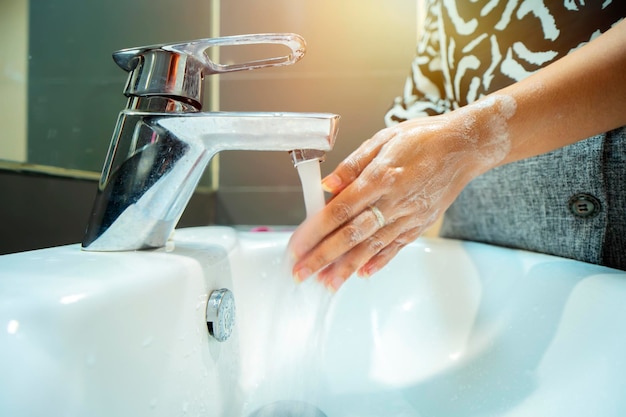 La donna usa il sapone e si lava le mani sotto il rubinetto dell'acqua dettaglio delle mani del concetto di igiene