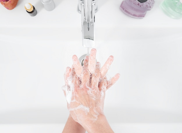 Женщина пользуется мылом и моет руки под краном воды. Концепция гигиены, вид сверху, здравоохранение. Личная гигиена и уход за телом