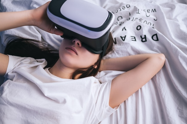 Woman use virtual reality glasses at home, relaxed on the bed. Plays games, technologies of the future