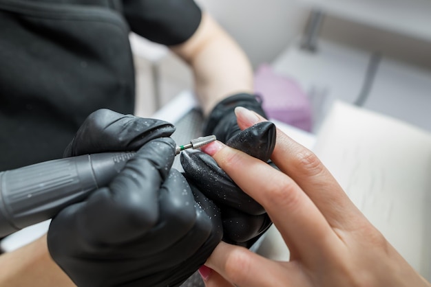 Una donna utilizza una lima per unghie con trapano elettrico in un salone di bellezza processo di manicure perfetto per unghie o intervento chirurgico nelle immediate vicinanze