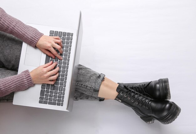여자는 흰색 배경에 노트북을 사용합니다 청바지와 부츠에 여성 다리 온라인 작업 상위 뷰