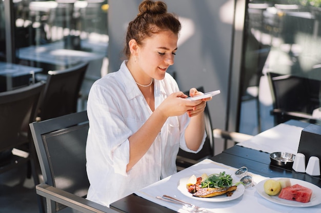 A woman uses a phone and eats lunch or breakfast outdoors in a cafe