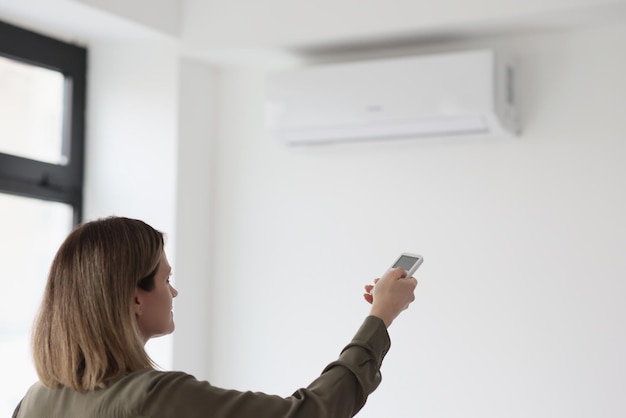 Woman uses remote control to adjust air conditioner in light office stabilization of