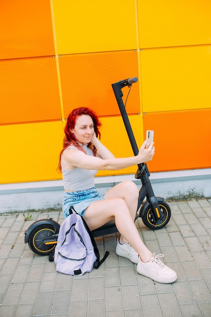 Woman uses a smartphone and an electric scooter in the summer in the city